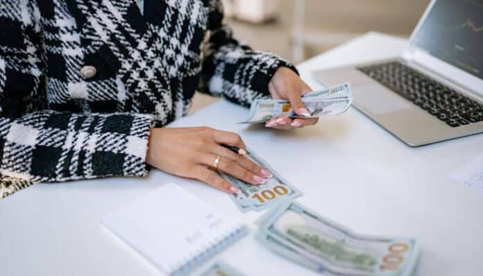 Person counting money with business loan strategy in focus, surrounded by cash and financial planning notes on a desk, symbolizing startup funding