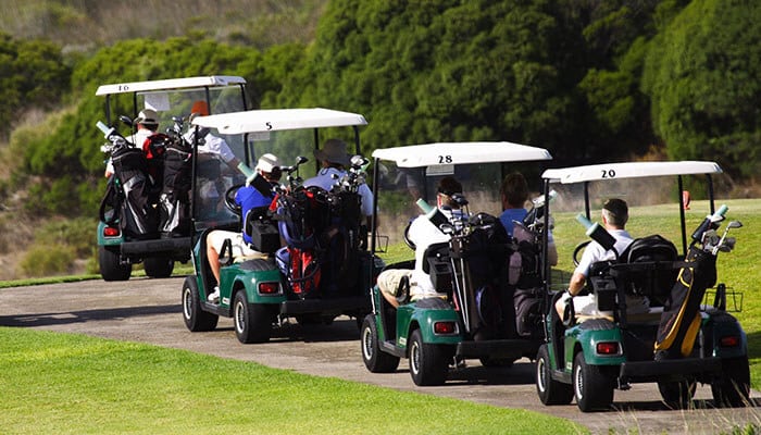 Multiple golf carts carrying players on a golf course, showing traditional uses for golf carts before their modern roles in communities and workplaces.