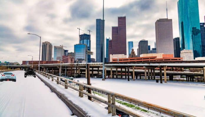 A snow-covered Texas highway with downtown skyscrapers in the background, highlighting the need for Texas' extreme weather preparedness for offices.
