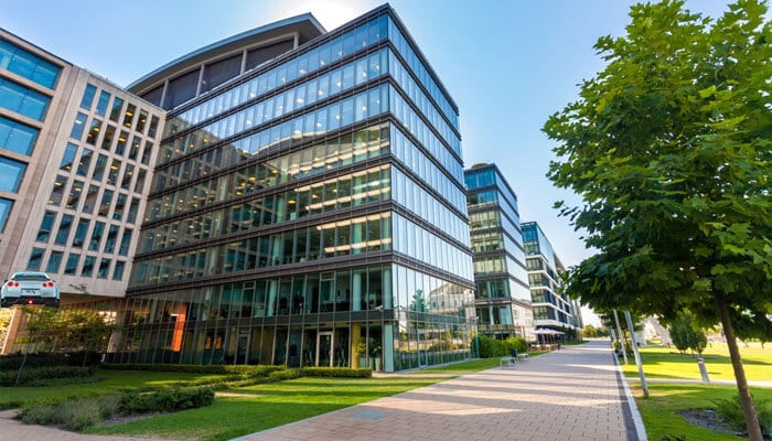 The modern glass office building surrounded by greenery, illustrating the importance of Texas' extreme weather preparedness for offices in protecting business properties.