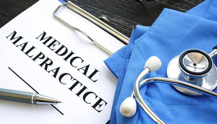 A document titled medical malpractice next to a stethoscope and surgical scrubs, representing personal injury cases related to medical malpractice