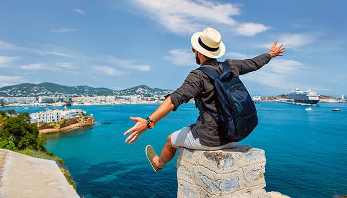 A happy traveler sitting on a cliff overlooking a beautiful European coastline, representing the joy and freedom of flying in business class to Europe.
