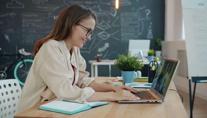 A woman learning online through a laptop in a creative workspace, illustrating how LXP vs LMS supports flexible and personalized workplace learning experiences.