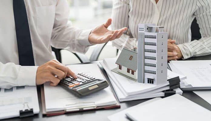 Insurance agents reviewing paperwork with calculator and building models on the table, illustrating factors that influence commercial building insurance costs.