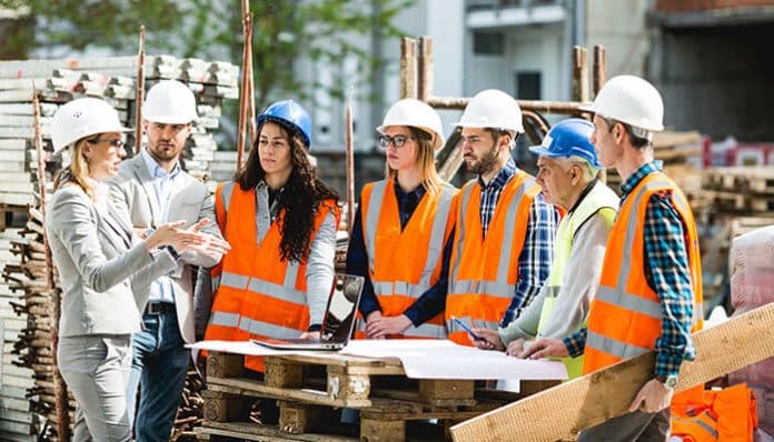 Team meeting at a worksite with engineers and workers in safety gear, illustrating teamwork in construction firms