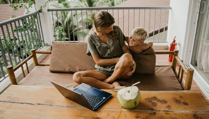 Parent working remotely on a laptop while sitting with a child, illustrating remote work monitoring in a flexible work environment.