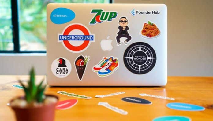 A laptop covered with colorful stickers, including 7UP and Underground, and a small plant, symbolizing creativity and the process to build a brand from scratch.