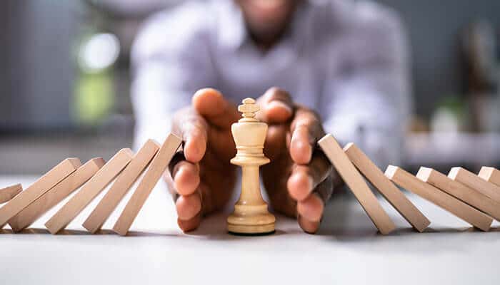Strategic decision-making represented by a hand protecting a chess king from falling dominos, symbolizing the careful planning needed when following Polygon announcements for smart investments.