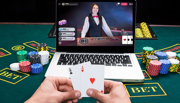 Technology Transformed Casinos showing a live dealer game on a laptop screen with poker chips, cards, and a player’s hand holding a pair of aces.