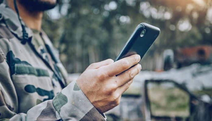 Soldier in camouflage using a smartphone, illustrating the implementation of Army BYOD strategies for secure communication and enhanced productivity in military operations