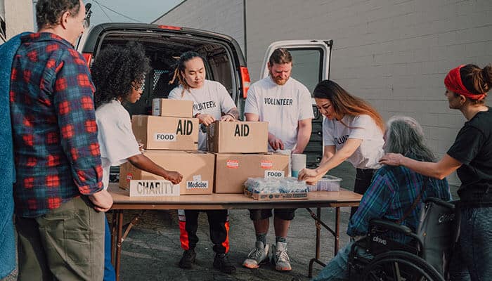 A group of volunteers unloading aid boxes labeled food and medicine from a van and organizing supplies on a table while supporting community outreach efforts through holiday corporate donations.