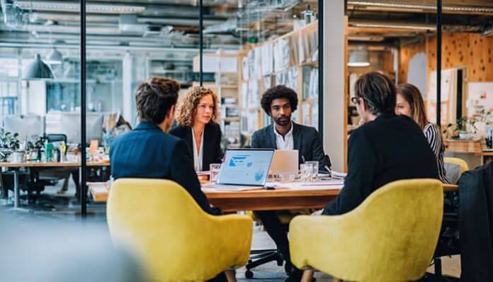 A team of professionals sitting around a conference table in a modern office discussing project plans on laptops illustrating how reliable startup booths internet supports seamless collaboration and connected workflows