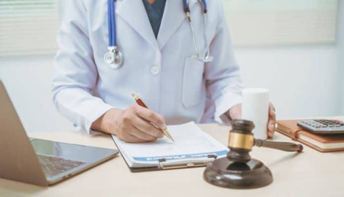 Doctor writing a Medico Legal Report at a desk with a gavel, laptop, and medical files