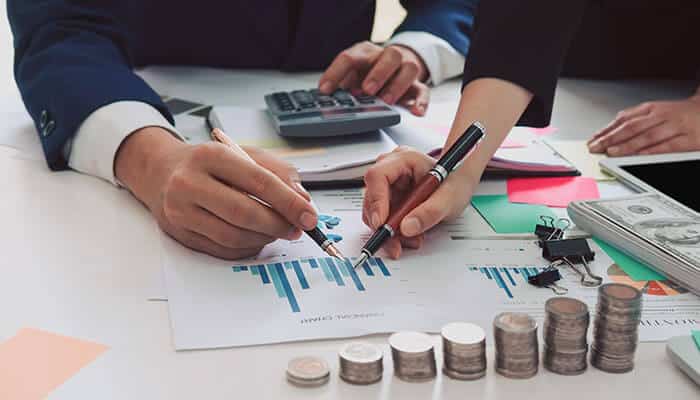 A close up view of business professionals reviewing financial charts with pens calculators and stacks of coins on the table highlighting the importance of reliable startup booths internet for smooth data analysis and decision making.