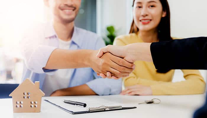 Two people shaking hands with a model house on the table, representing a successful real estate transaction for first-time buyers when buying your first Dubai apartment.