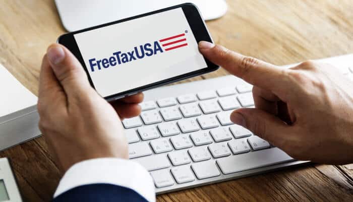Person using FreeTaxUSA on a smartphone while sitting at a desk with a keyboard, highlighting the tax filing service.