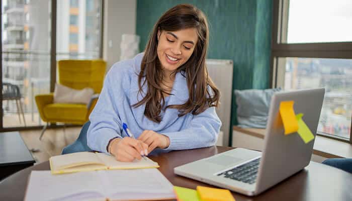 Soft Skills In Online Undergraduate Education shown by a student studying online, taking notes, and developing communication and critical thinking skills.