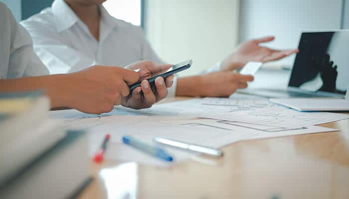 Close-up of hands holding a smartphone and credit card, working on a laptop surrounded by business plans and sketches, highlighting SEO strategy and digital marketing