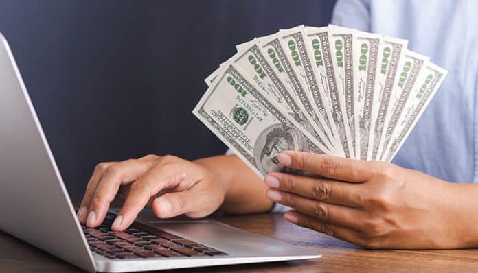 Person holding cash while working on a laptop, exploring online business ideas to make money online