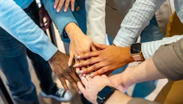 Juntos seguros concept illustrated through a diverse group of professionals stacking hands together in a team unity gesture, symbolizing collaborative resilience, shared responsibility, and collective security strategies used in modern organizational and community risk management systems.