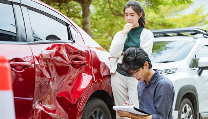 A woman observing an employee car accidents while an insurance agent documents the damage