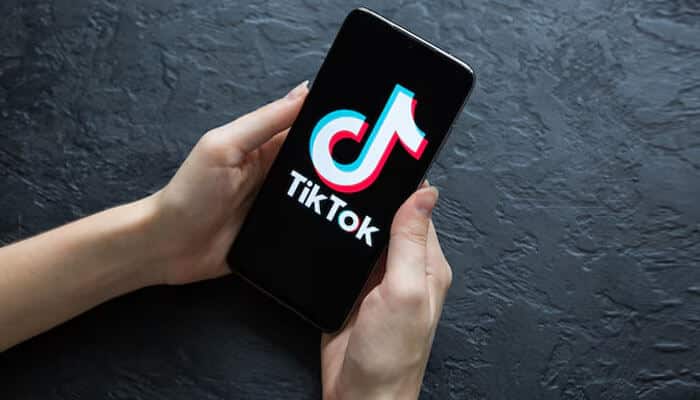 What Is TikTok Wrapped - Startupeditor | Startup Editor TikTok Wrapped concept image featuring a person holding a smartphone with the TikTok logo on screen against a dark background.