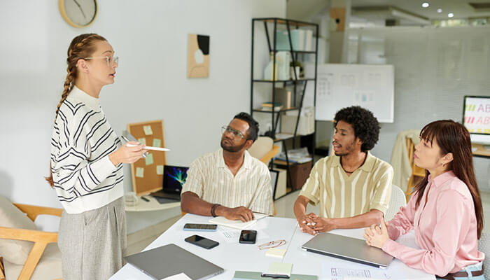 Build a Funding Structure That Actually Works - Startupeditor | Startup Editor Woman presenting to three coworkers around a table in a bright office, with laptops and papers visible on the desk.