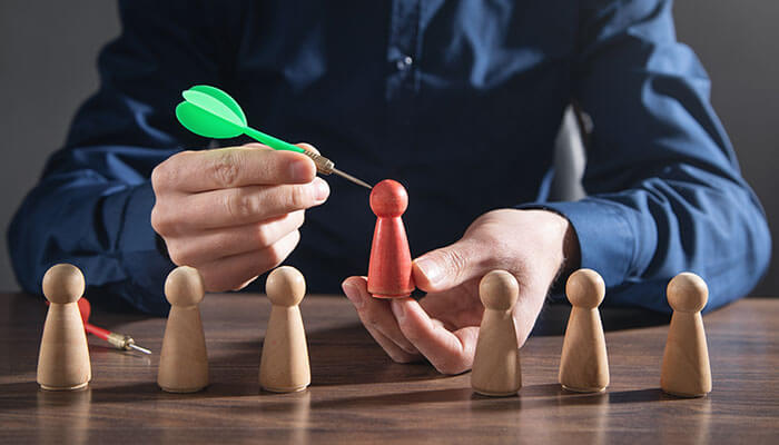 Define Your Target Audience Carefully - Startupeditor | Startup Editor Marketer aiming a dart at a highlighted audience figure, representing audience targeting in how to run paid social media ads.