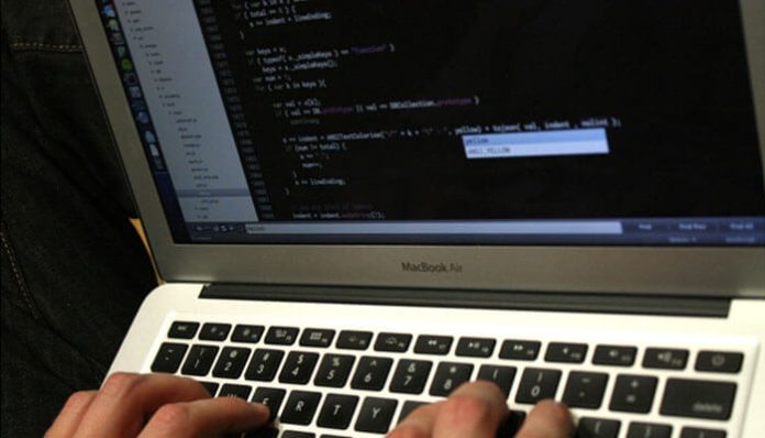 Person typing on a MacBook Air with lines of code on the screen, in a code editor window.