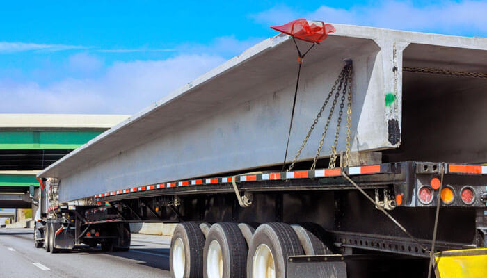 Key Factors That Determine Fault - Startupeditor | Startup Editor Semi-trailer carrying a large concrete beam on a highway, secured with chains and a red tarp edge visible on top.
