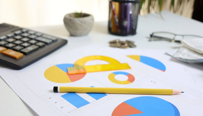 Strategic Benefits of Automated Workflows - Startupeditor | Startup Editor Office desk with colorful pie charts on papers, a yellow pencil resting on top, and a calculator nearby.
