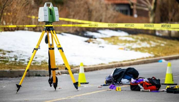 Surveying tripod with a leveling instrument on a taped-off street; scattered bags and cones indicate a crime or accident scene.