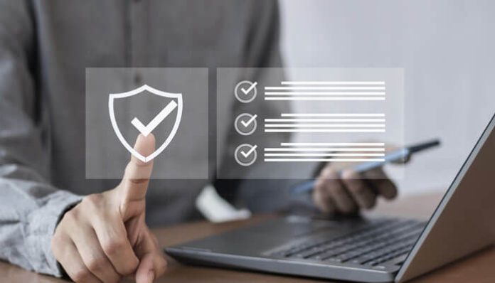 Person using a laptop with a translucent security shield and checklist overlay, symbolizing cybersecurity and compliance.