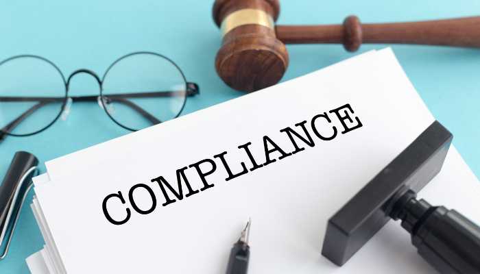 Compliance Will Become a Product Category | Startup Editor Document labeled COMPLIANCE on a blue desk with a gavel, glasses, pen, and stamp nearby (legal/regulatory context).
