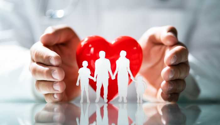 Group Health Insurance | Startup Editor Hands cradle a red heart surrounding a white cutout of a family holding hands, symbolizing protection and care for loved ones.