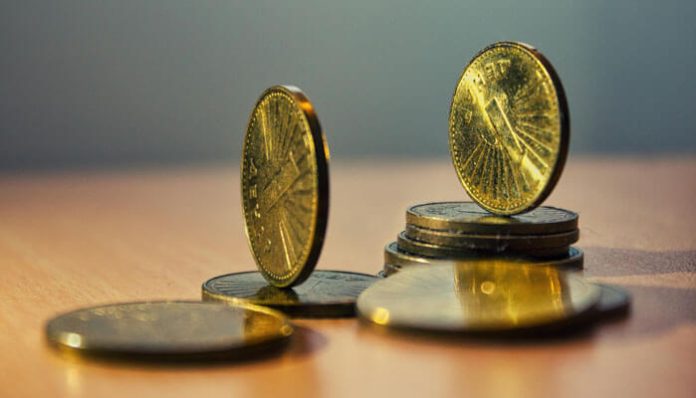 Close-up of gold and silver coins stacked and balanced on a wooden surface, with one coin leaning on edge in the foreground.