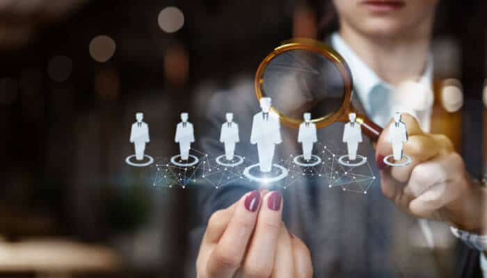 Frameworks to Drive Performance - Startupeditor | Startup Editor Person holding a magnifying glass over a row of small white human figures connected by a network, symbolizing talent search or recruitment.