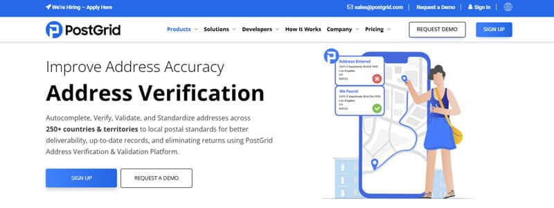 PostGrid Address Verification - Startupeditor | Startup Editor Illustration of a woman beside a large smartphone displaying a map and address verification icons in a PostGrid hero section.