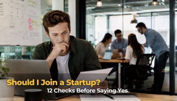Professional considering “Should I Join a Startup?” while working on a laptop in a busy startup office.