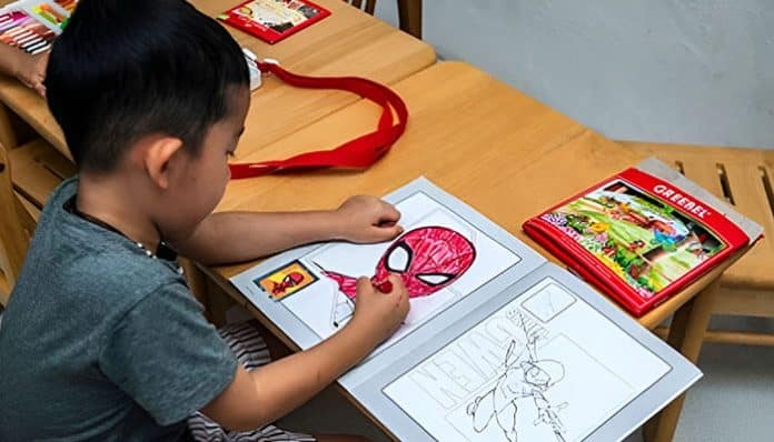 Child coloring a Spiderman Coloring Page with crayons at a classroom desk