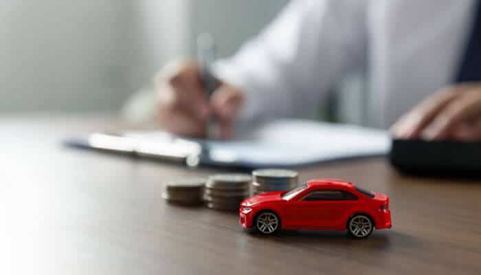 What Is Negative Equity on a Car Loan - Startupeditor | Startup Editor Toy car, coins and loan paperwork representing dealerships that will pay off your trade no matter what you owe.
