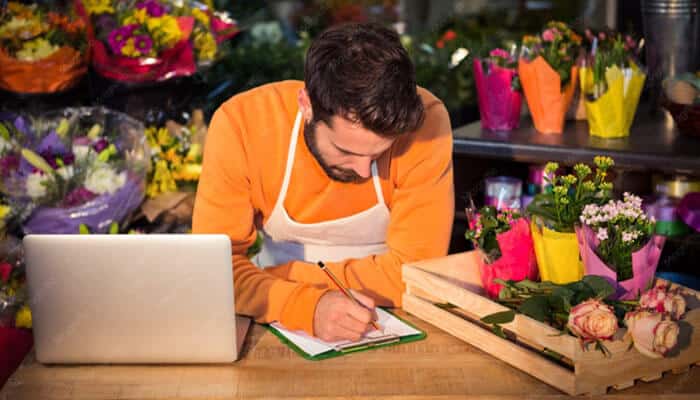 Where Blog ThriftyEvents.net Could Improve - Startup Editor | Startup Editor Blog ThriftyEvents.net florist working beside a laptop while planning floral arrangements, vendor tasks and event decoration costs.