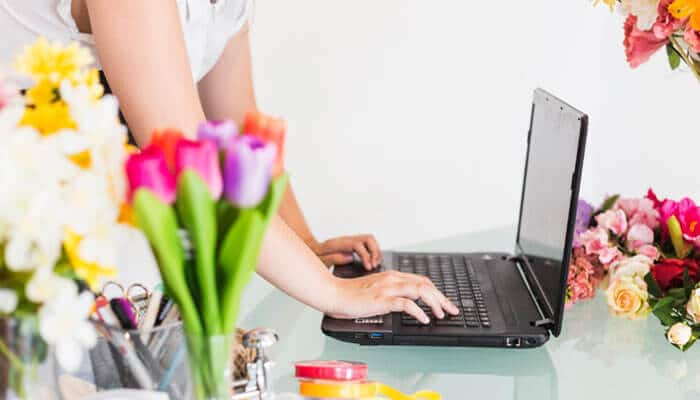 The Business Idea Behind Blog ThriftyEvents.net - Startup Editor | Startup Editor Blog ThriftyEvents.net event planner using a laptop beside colorful flowers while organizing décor, budgets and celebration details.