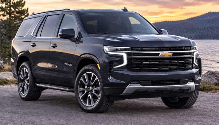 2027 Chevy Tahoe - Startupeditor | Startup Editor 2027 Chevy Tahoe black SUV parked beside a lake with mountains and sunset in the background.
