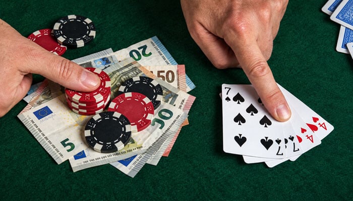 Poker Hands Ranked: Hand Probabilities - Startup Editor | Startup Editor Poker player revealing a pair of sevens beside casino chips and euro banknotes during a card game.