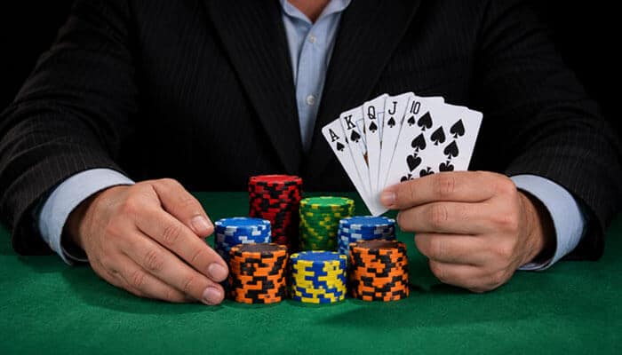 Poker Hands Ranked: The Best Five-Card Rule in Texas Hold'em - Startup Editor | Startup Editor Poker player holding an ace-high royal flush in spades behind stacks of colorful casino chips on a green felt table.