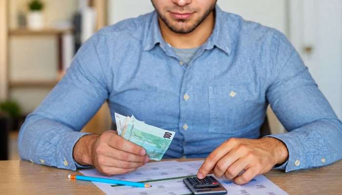 Common Types of Spiff Payments - Startup Editor | Startup Editor Man calculating a Spiff Payment with a calculator, cash, and financial documents to review sales incentives and expected earnings.