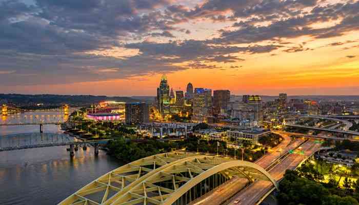 How Businesses Can Use the Cincinnati Business Courier - Startup Editor | Startup Editor Cincinnati Business Courier regional business coverage illustrated by the Cincinnati skyline, Ohio River bridges, and illuminated buildings at sunset.