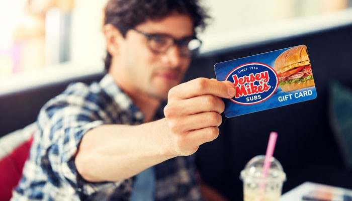 What If a Jersey Mike's Gift Card Doesn't Work? - Startup Editor | Startup Editor A customer holding a Jersey Mike's Gift Card at a restaurant table, showing the branded prepaid card used for sandwich purchases.