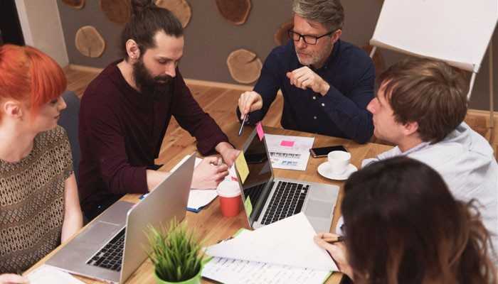 How to Apply for HubSpot for Startups - Startup Editor | Startup Editor HubSpot for Startups business team collaborating around laptops and documents while planning CRM, marketing, sales, and customer growth strategies.